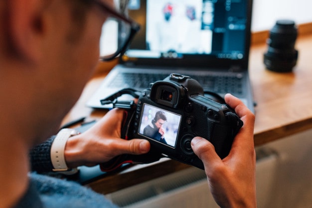 male hands holding professional camera looks photos sitting cafe with laptop 8353 6240 min